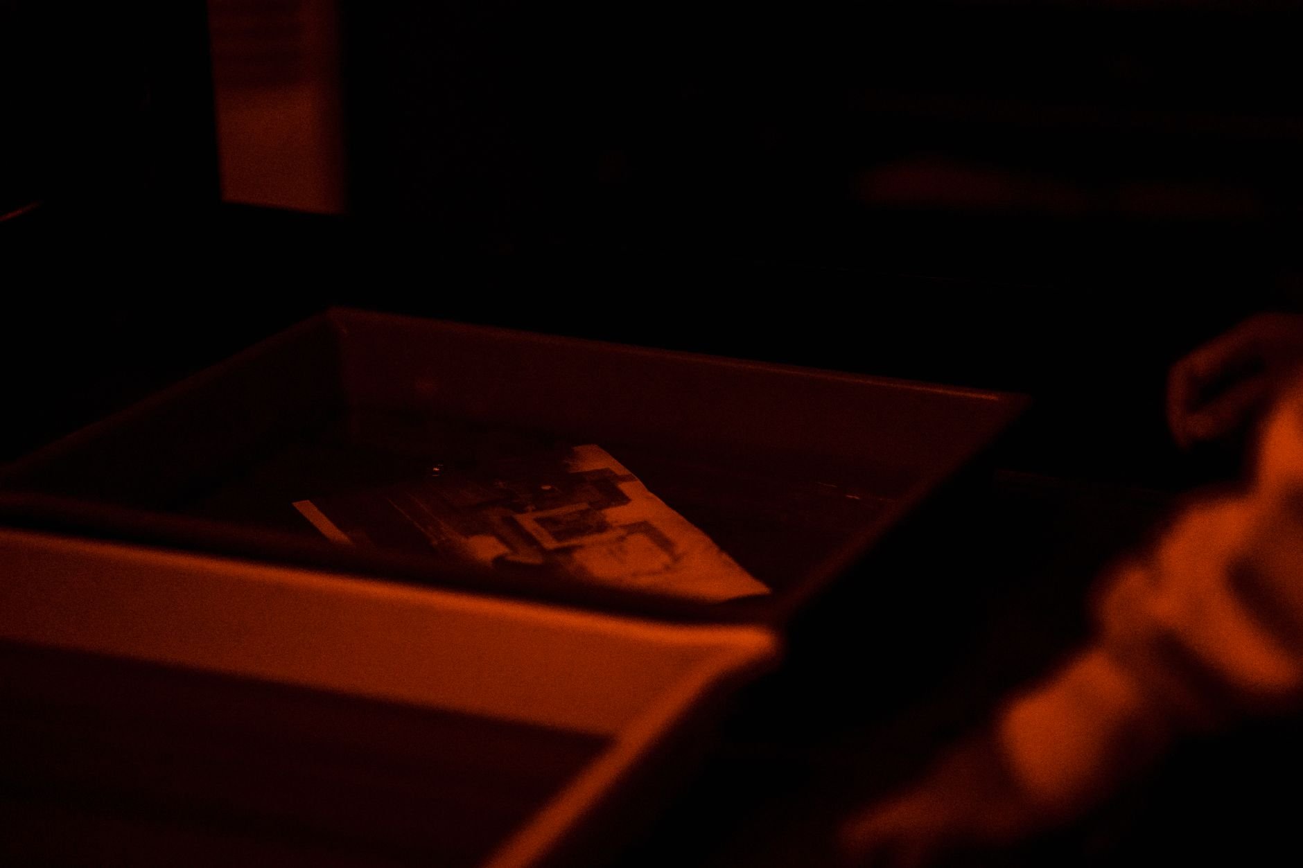 Moody scene of photo developing in a darkroom under red light ambiance.